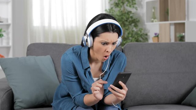Amazed woman listening to music from smart phone sitting on a sofa at home