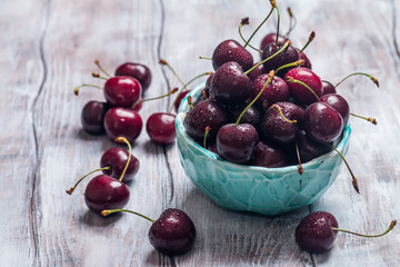 Cherries in a bowl with water drops close up on white wooden background