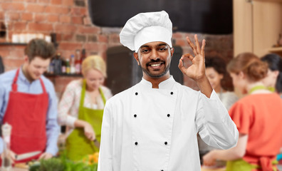 cooking class, profession and people concept - happy male indian chef in toque showing ok gesture over group of students background