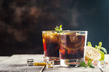 Fresh made Cuba Libre with brown rum, cola, mint and lemon on wooden background