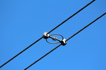 Two power line utility black electrical wires held together with strong insulators and spacers on clear blue sky background