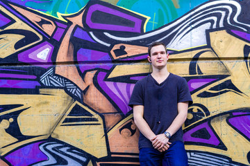 Junger Mann lehnt an Graffiti Mauer
