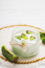 Yogurt with kiwi slices on a wooden white background.