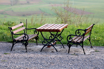 Wooden table and public benches with black metal baroque style support frame mounted on gravel...