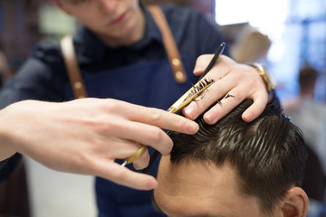 grooming, hairdressing and people concept - close up of male client and hairdresser with comb and scissors cutting hair at barbershop