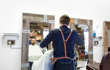 grooming, hairdressing and people concept - hairdresser cutting male client's hair at barbershop