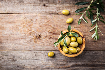 Fresh green olives in a bowl and olive branch on rustic wooden background, top view