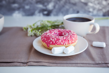 Glazed donut with black coffee and marshmallows. Pink tasty donut on a table. Morning breakfast.