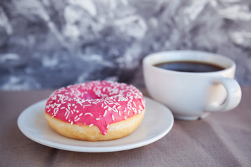 Glazed donut with black coffee and marshmallows. Pink tasty donut on a table. Morning breakfast.