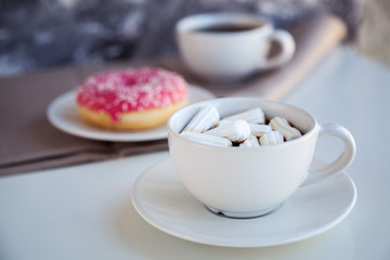 Fototapeta na wymiar Black coffee with glazed donuts and marshmallow. Pink tasty donut on a table. Morning breakfast.