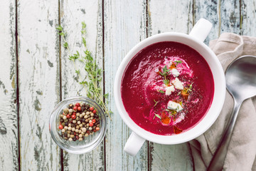 Cold Beetroot mashed soup with cream, apple, cheese and thyme in a white bowl over wooden background, top view.