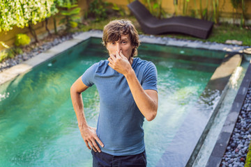 Young man with disgust on his face pinches nose, something stinks, very bad smell in swimming pool...