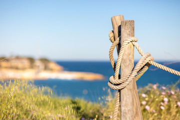 On an afternoon at the Mediterranean on the bay of Cabo Roig with a rope post standing on the edge of the high cliff overlooking the blue sea with beautiful bokeh.
