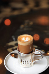 Small shot of espresso with steamed hot milk and cream on cafe table with light bokeh on background.