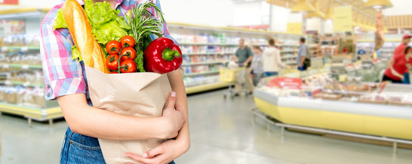 Smiling happy woman enjoying shopping at the supermarket, holding vegetables in eco friendly bag