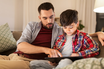 family, fatherhood, technology and people concept - father and little son with tablet pc computer sitting on sofa at home