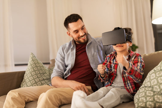 family, virtual reality and entertainment concept - happy father and little son in vr glasses playing video game at home