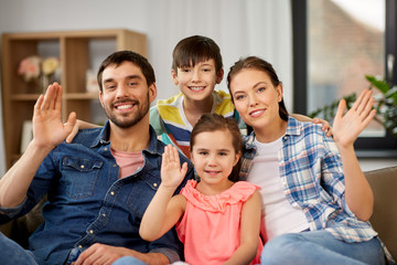 family and people concept - portrait of happy father, mother, little son and daughter waving hands at home