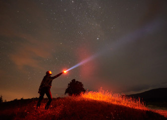 Silhouette of woman standing against night starry sky in the mountains with a lamp in his hand