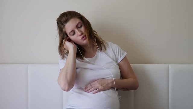 pregnant woman in a white t-shirt sitting on the bed at home