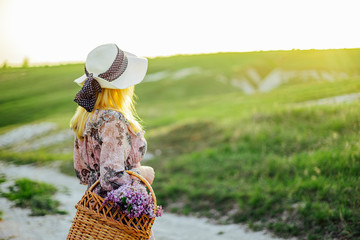 Young girl blonde in a hat and with a basket of flowers in a dress