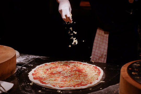 The chef sprinkles pizza with mazzarella cheese On a black background 