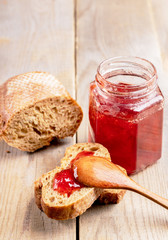 Fresh bread and jar with homemade strawberry jam on rustic wooden table.