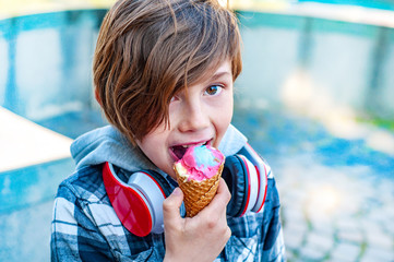 Fashionable boy eating multicolored ice cream in a waffle cone. Cool in the summer heat. Sweet snack