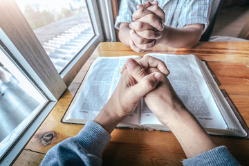 Two christian sitting around wooden table with praying to God together on holy Bible.