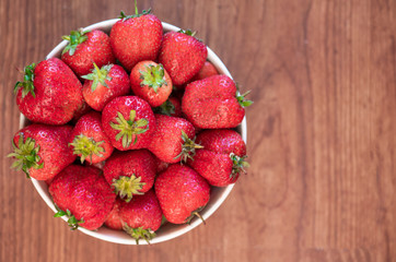 Fresh organic strawberry in the white bowl, on the wooden background. 