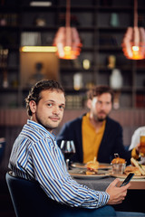 Young arab man dressed smart casual sitting at dinner in restaurant and using smart phone.