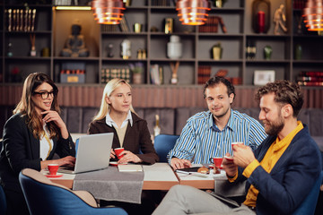 Group of multiethnic colleagues sitting at restaurant and talking about new project. Start up business concept.