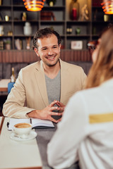 Two multicultural smiling colleagues dressed smart casual sitting in restaurant and discussing about project.