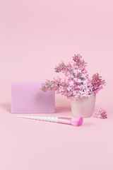 Feminine accessories with unicorn makeup brushes on pink background and trendy lilac  flowers branch with a card. copy space, birthday beauty and cosmetics blogger concept
