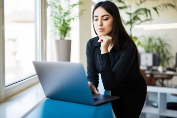 Concentrated young beautiful business woman working on laptop in modern office