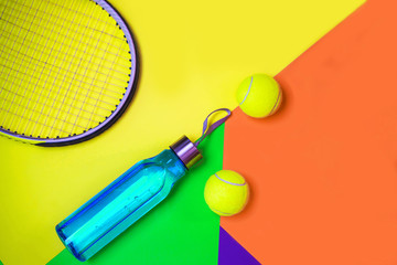Tennis layout with tennis balls, racket, bottle of water on abstract different multicolored neon background with place for text. Sport concept with tennis play. Flat lay, top view, selective focus.
