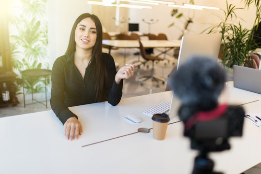 Cheerful young woman blogger recording video with camera in modern office