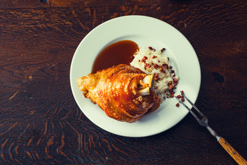 Crispy roasted pork knuckle. Schweinshaxe, roasted ham hock with cabbage salad and sauce on a plate on wooden table