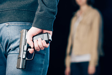 cropped view of criminal hiding gun while standing near woman on black