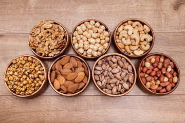 Different mixed nuts in a  bowls on wooden table. Healthy food and snack.