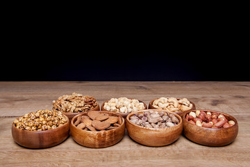Different mixed nuts in a  bowls on wooden table. Healthy food and snack.