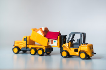 Obraz na płótnie Canvas Miniature forklift truck lifting up mini house using as property real estate and industry concept