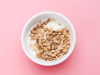 Whole grains on yogurt in white bowl, pink background.