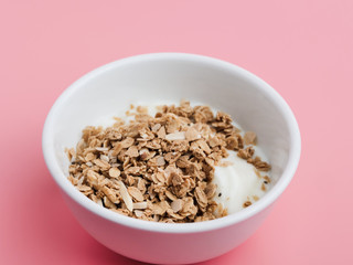 Whole grains on yogurt in white bowl, pink background.