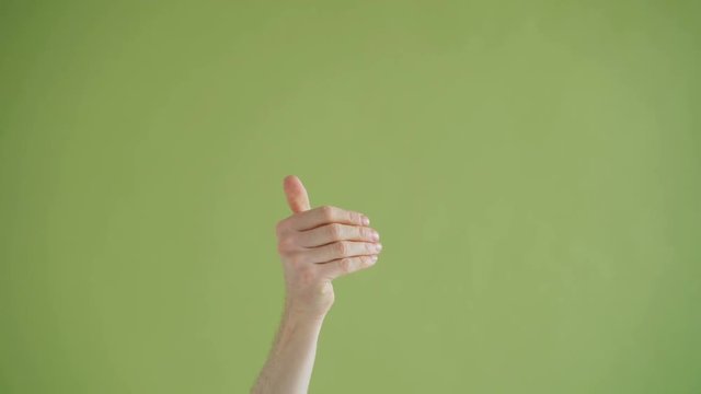 Close-up shot of male human hand pointing finger at camera then waving inviting to join on green background. Body language and communication concept.