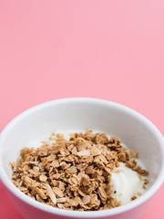 Whole grains on yogurt in white bowl, pink background.