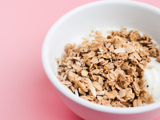 Whole grains on yogurt in white bowl, pink background.