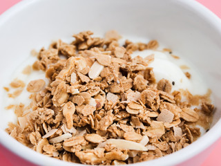 Whole grains on yogurt in white bowl, pink background.