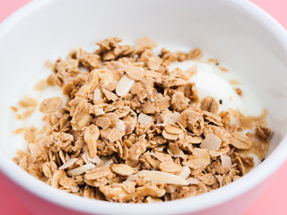 Whole grains on yogurt in white bowl, pink background.