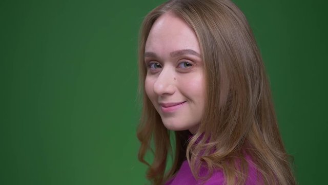 Portrait of beautiful ginger student turns to camera watching with shy smile into it on green chroma background.